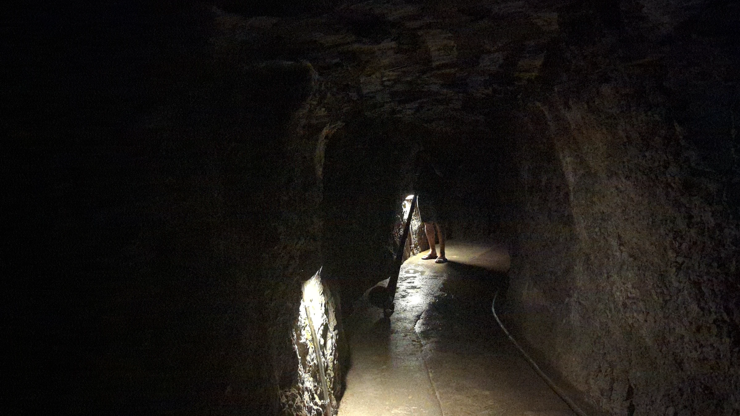 Alphornbläser in einem schwach beleuchteten Tunnel der Aareschlucht am Abend, der Becher des Alphorns liegt auf dem Weg