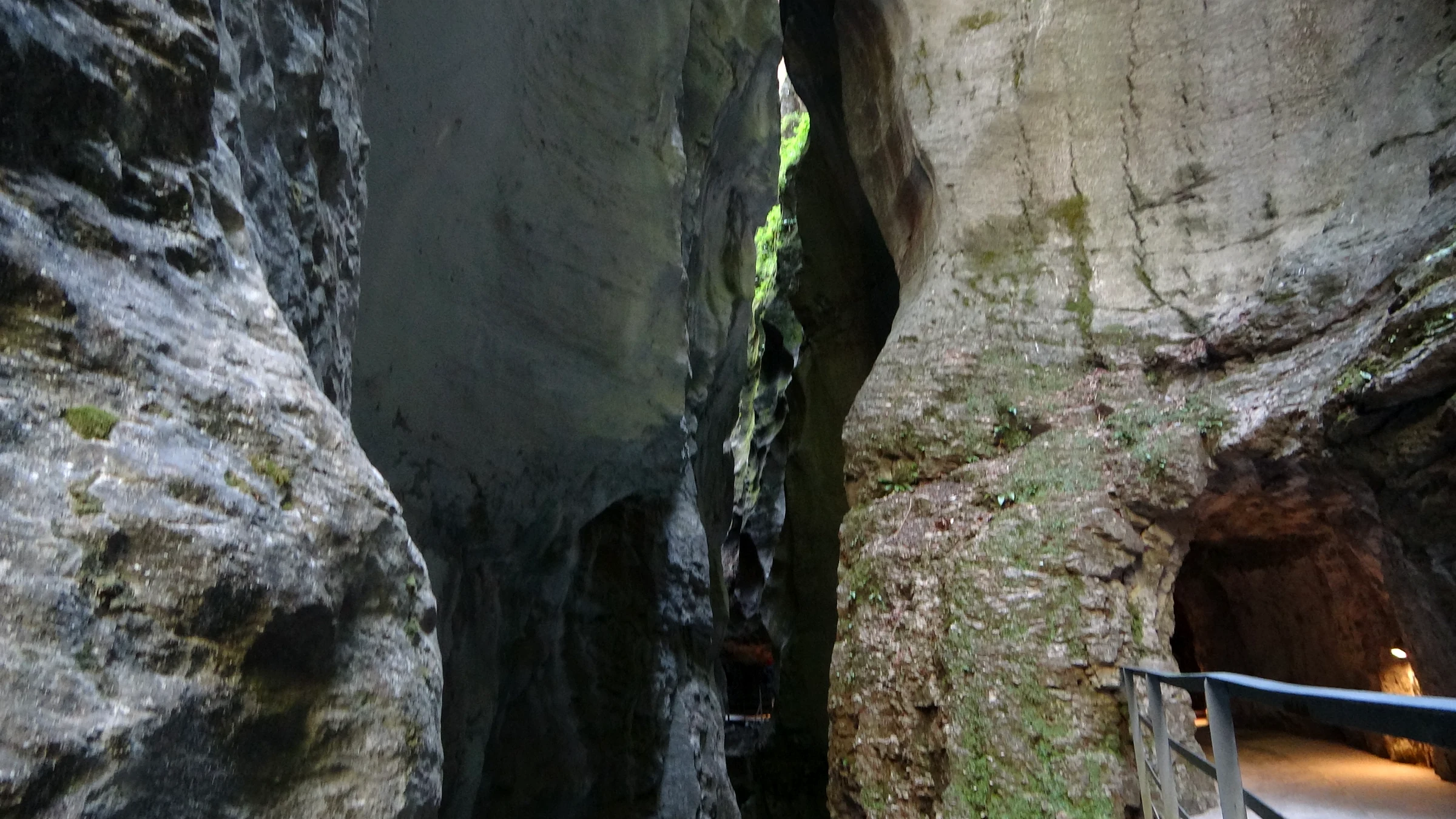 Beleuchteter Tunneleingang in der Felswand der Aareschlucht mit dem Steg davor
