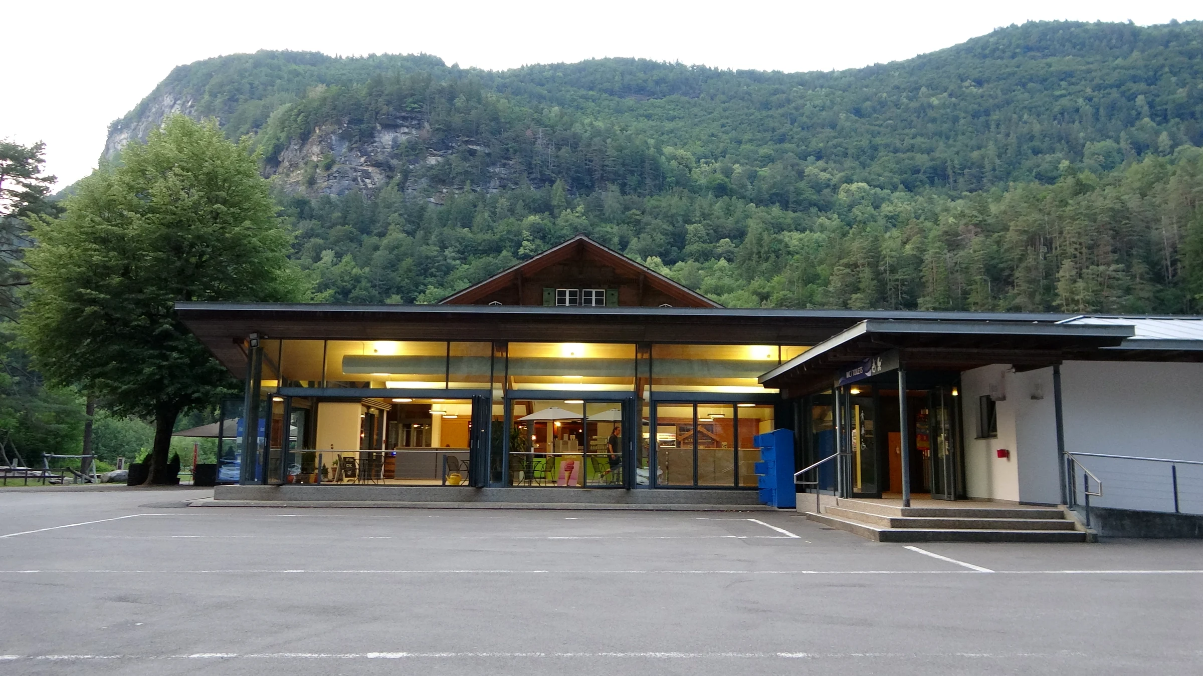 Beleuchtete Gebäude am Eingang West der Aareschlucht in der Dämmerung, fast leerer Parkplatz