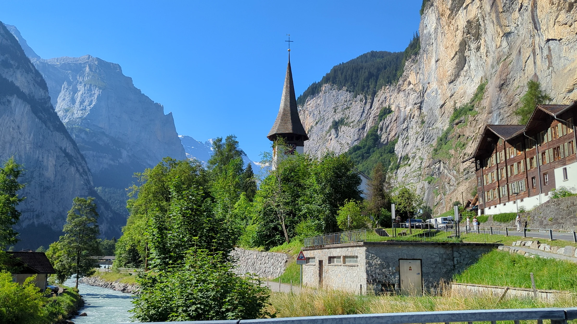 Kirche von Lauterbrunnen und Staubbachfall unter blauem Himmel an einem ruhigen Julimorgen