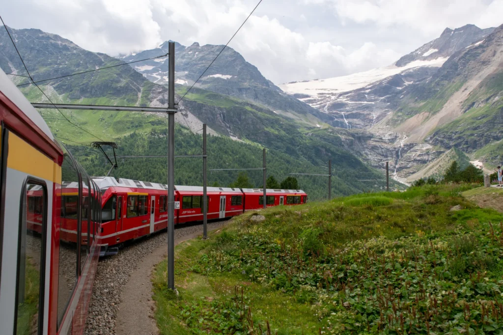 Bernina Express leaving Alp Grüm station in a sharp curve with the valley and mountains behind