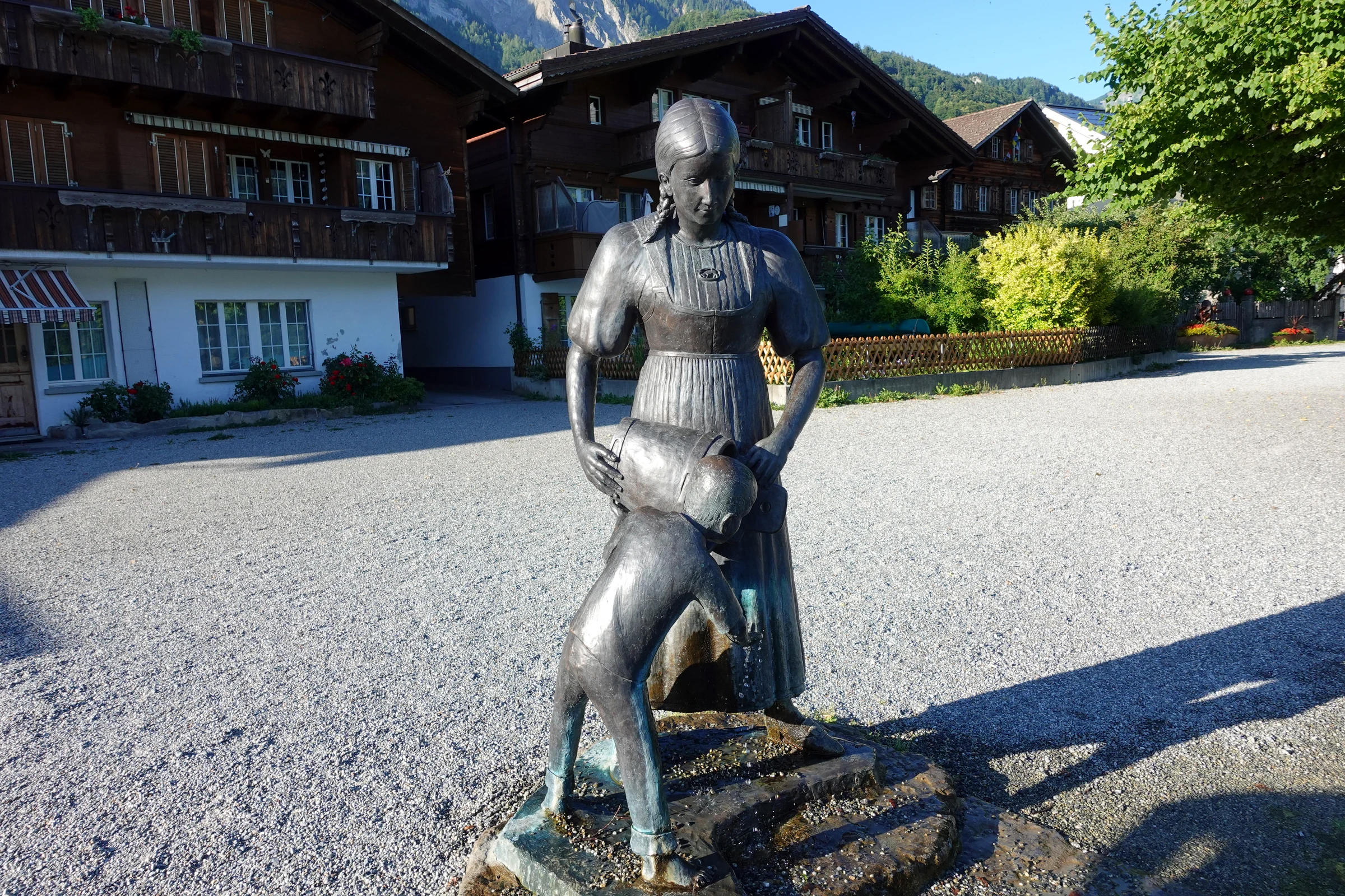 Bronzeskulptur auf einem Kiesplatz am See in Brienz, dahinter alte Holzhäuser