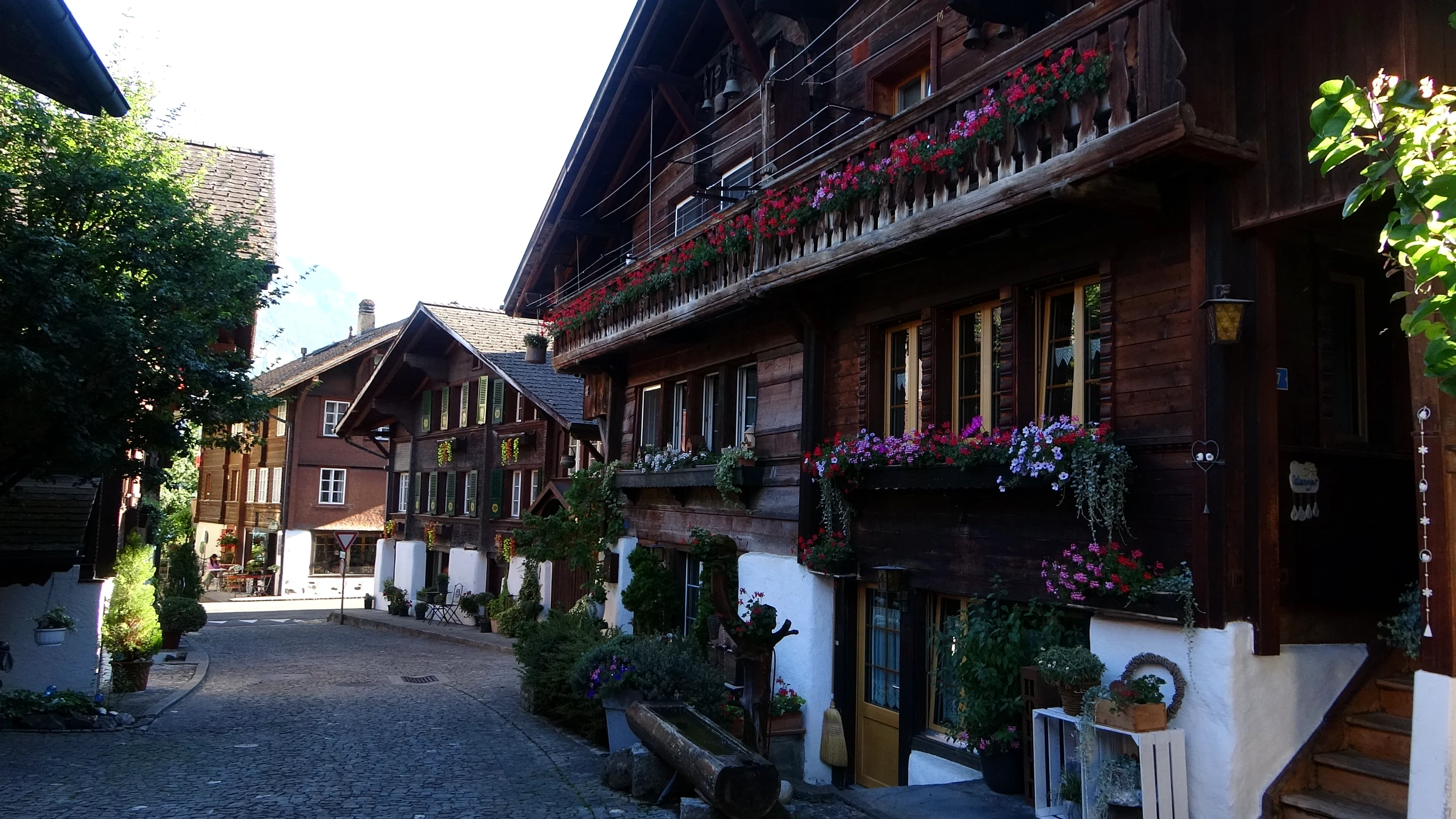 Gepflasterte Gasse zwischen alten Holzhäusern mit Blumenkästen und Bänken in Brienz