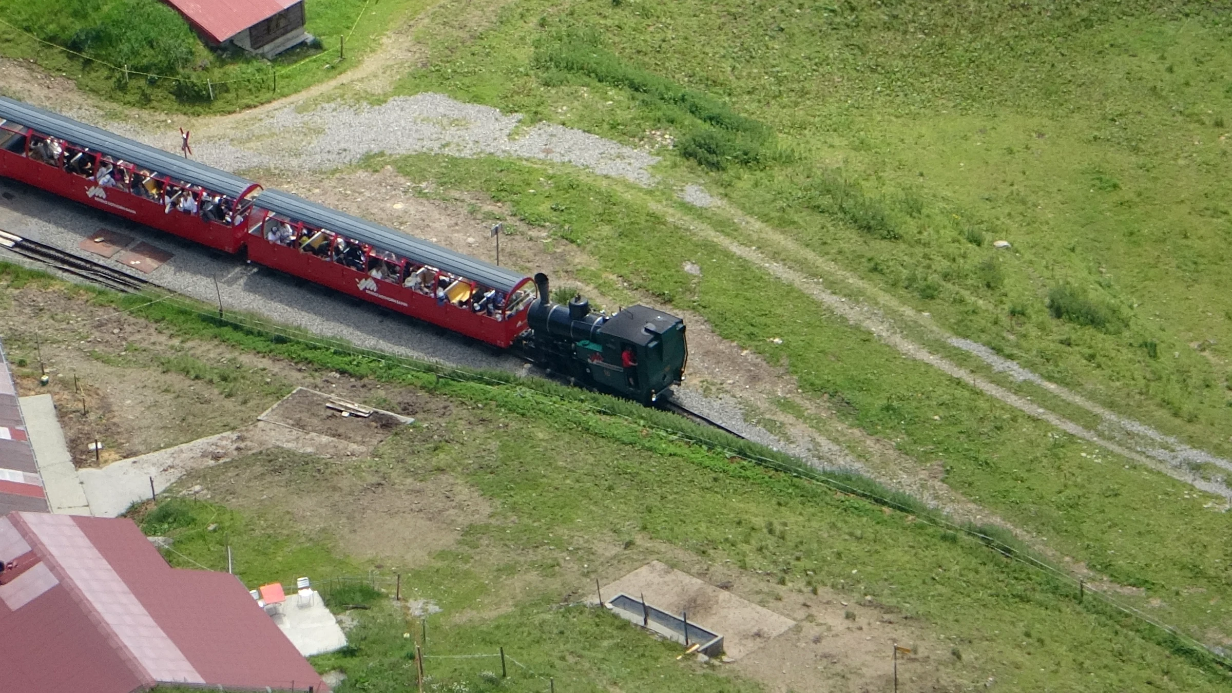 Dampfzug der Brienz Rothorn Bahn fährt an einer Alphütte unterhalb des Brienzer Rothorns vorbei, von oben gesehen