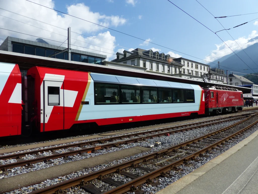 Glacier Express train in Brig station with a light-coloured Excellence Class carriage between the red panoramic cars