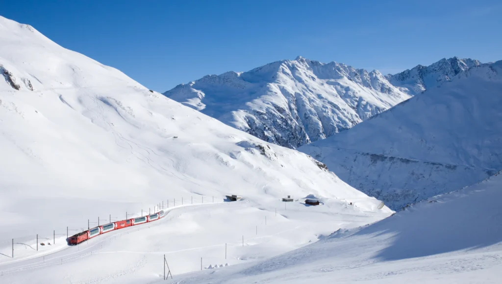 Roter Glacier Express im tiefen Schnee unterhalb des Oberalppasses unter blauem Himmel