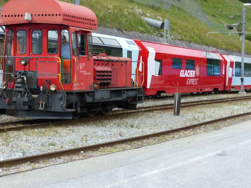 Red and white Glacier Express panoramic carriages parked at Zermatt station with mountains behind
