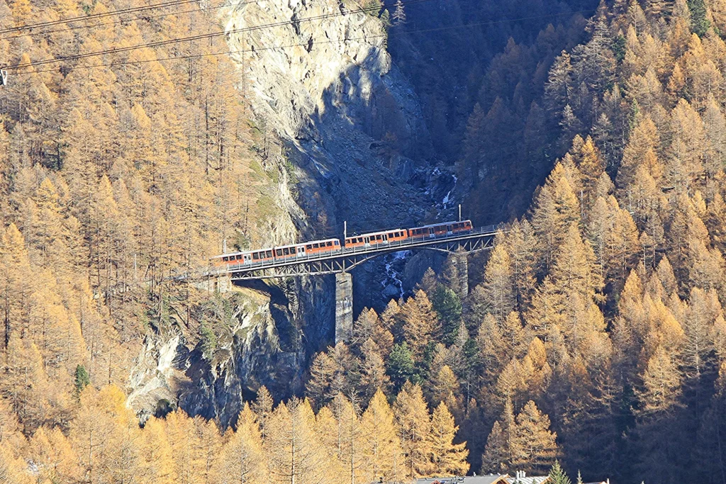 Gornergrat train crossing the curved Findelbach viaduct above a gorge with golden autumn larches