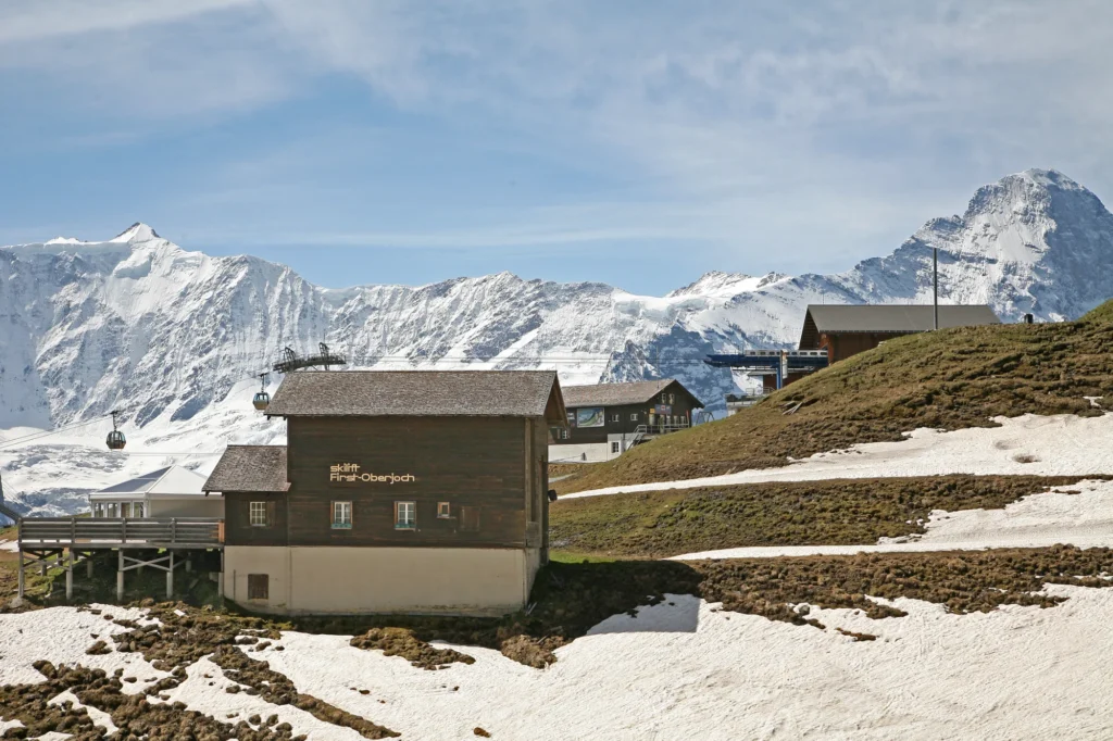 Mountain station and wooden restaurant at Grindelwald First on a sunny day with snowy peaks behind