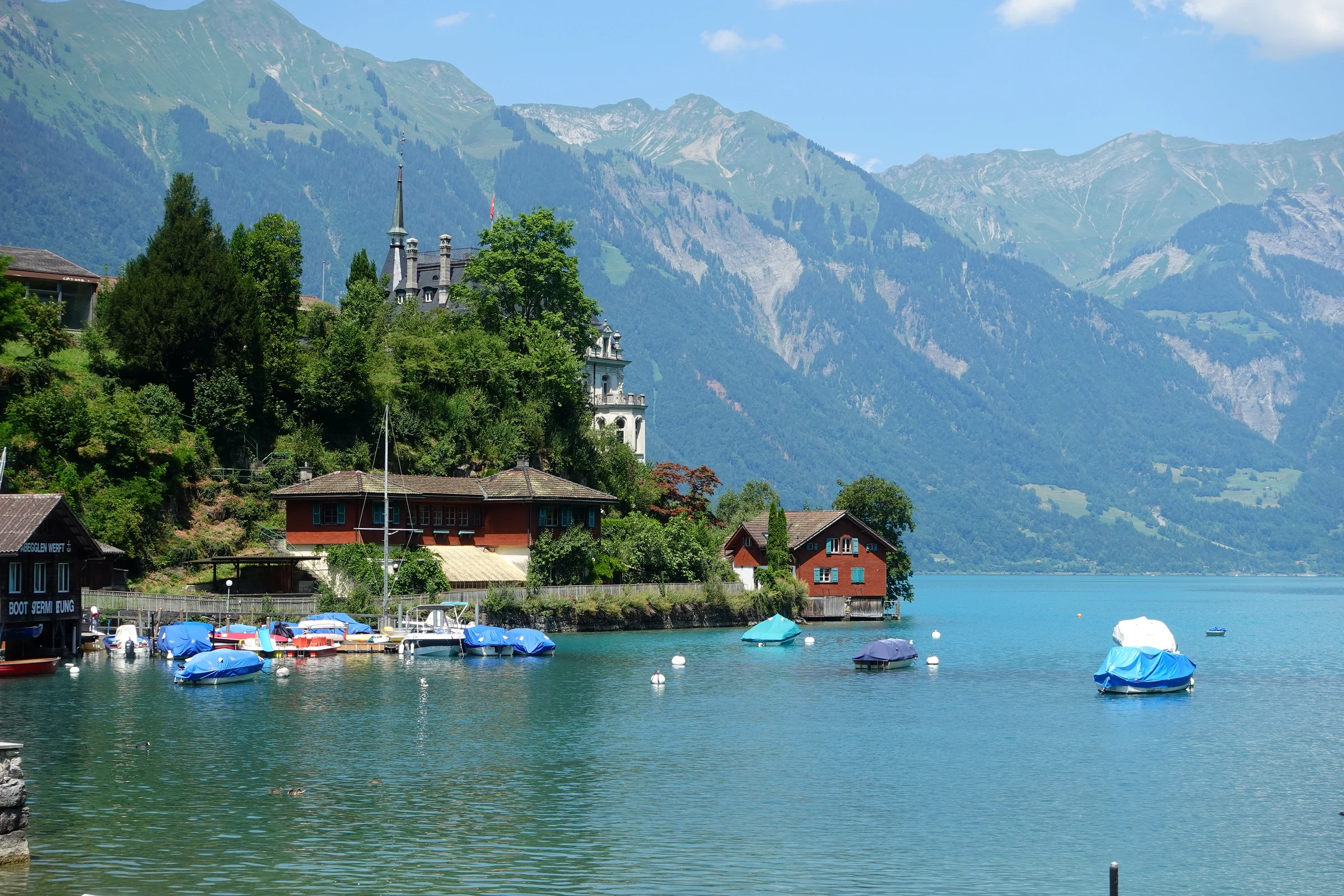 Small boats moored in the bay of Iseltwald below the wooded peninsula with the castle tower