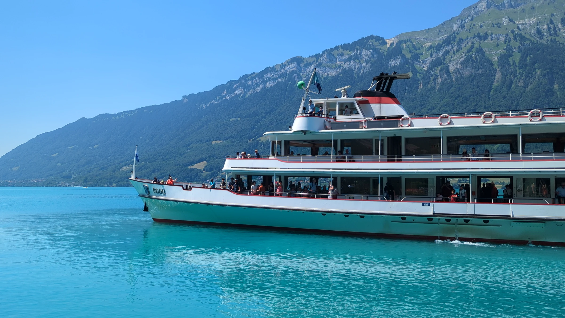 The white BLS motor ship MS Brienz cruising on turquoise Lake Brienz after leaving Iseltwald