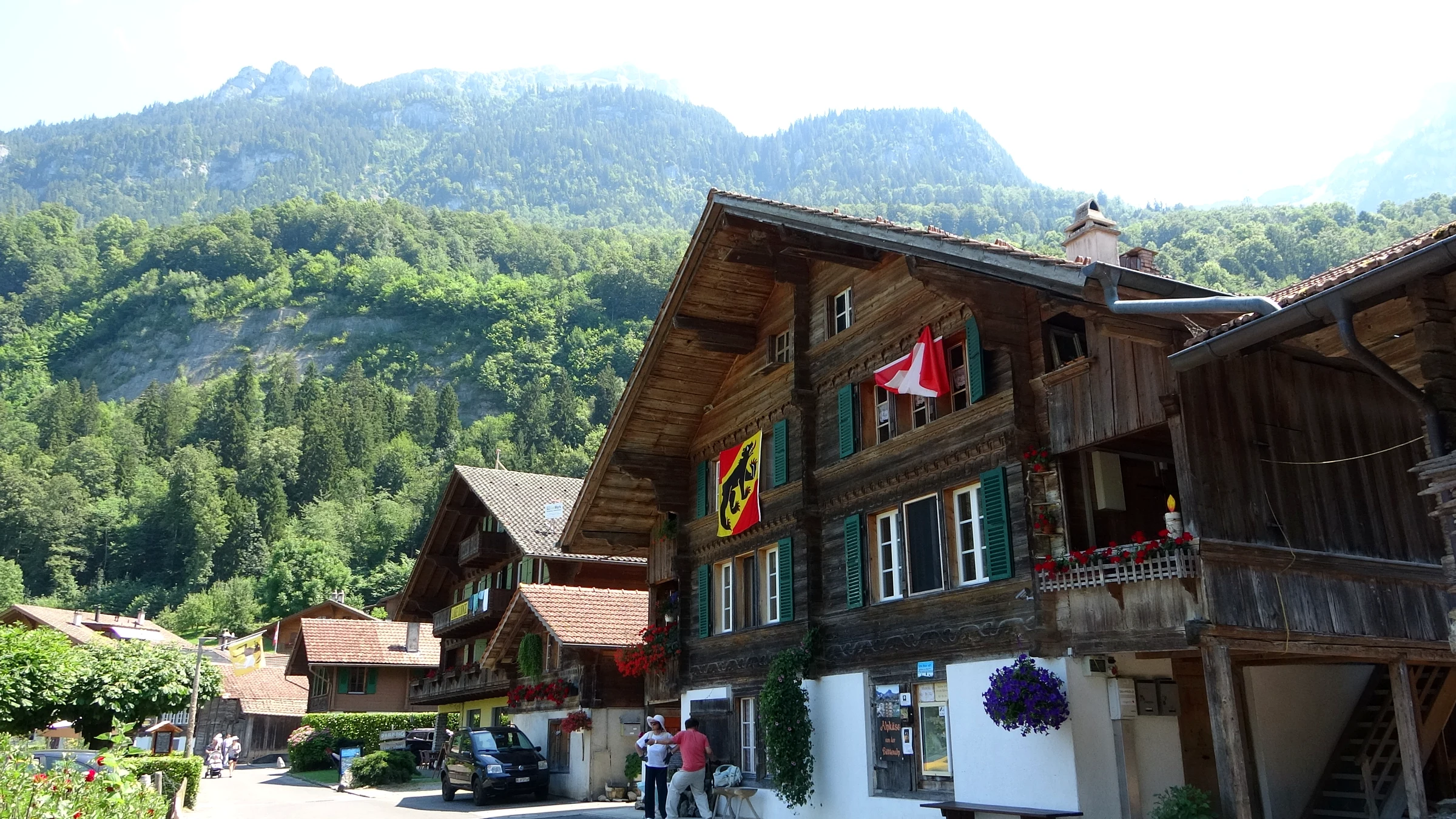 Old wooden chalets with flower boxes and Swiss and Bernese flags in the main lane of Iseltwald