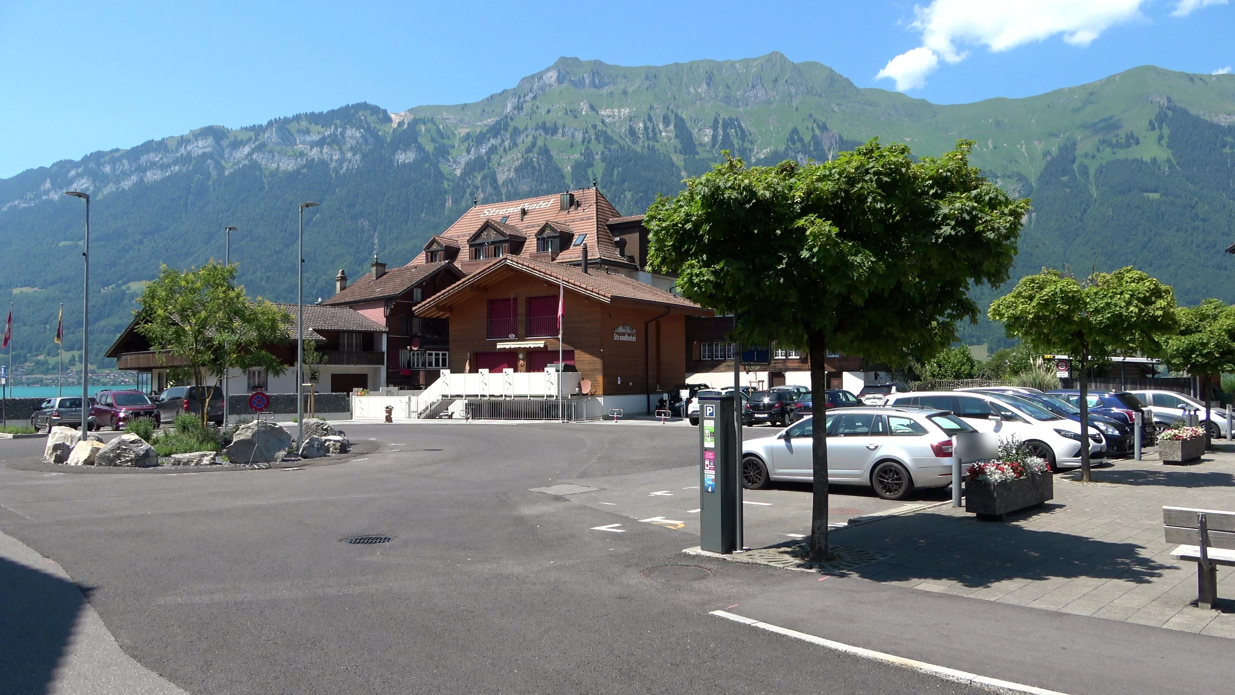 Parking pay station at a car park in the centre of Iseltwald with the Strandhotel and the mountains behind