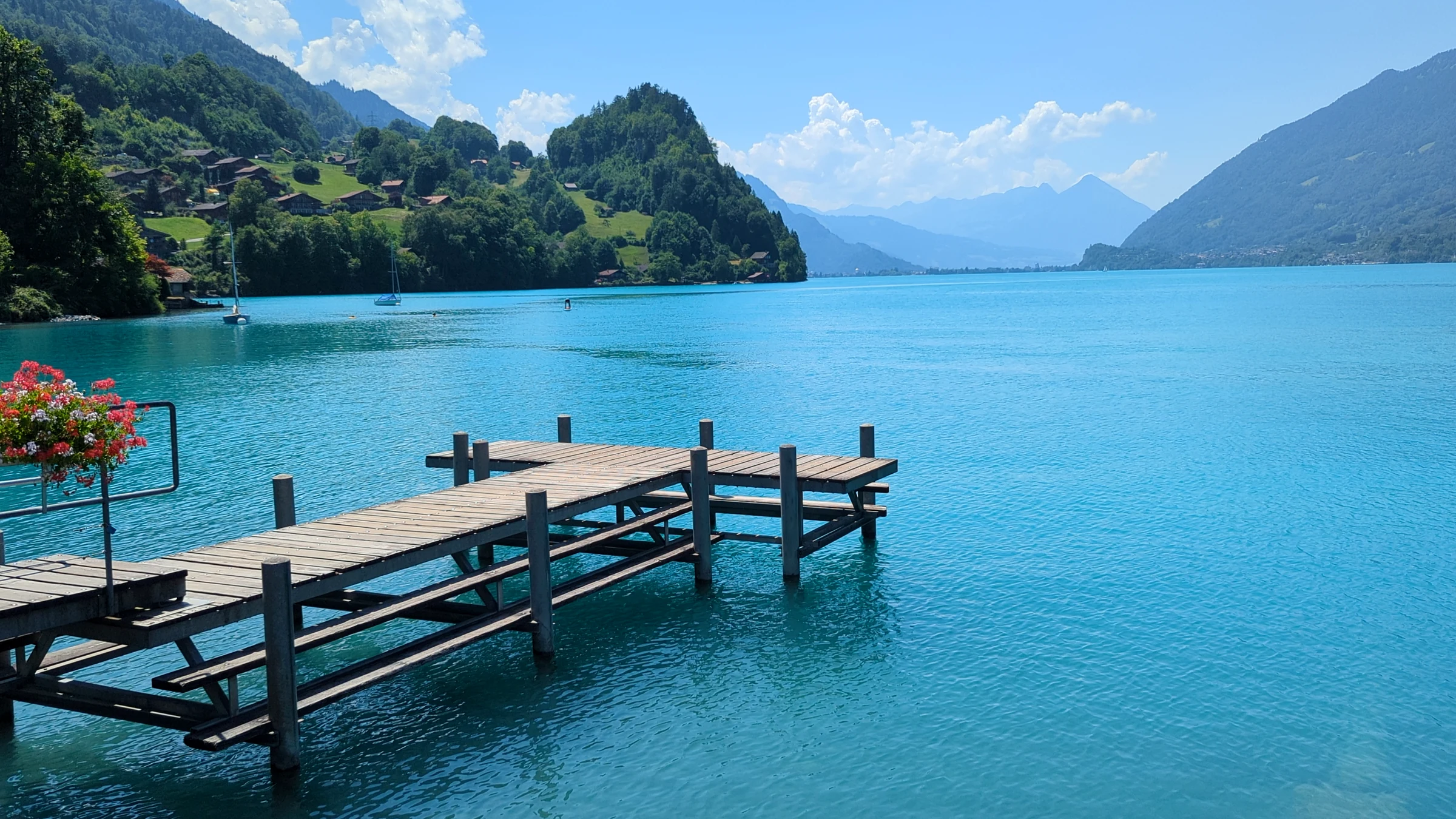 The empty Iseltwald pier with red geraniums at the railing and the turquoise lake stretching towards Interlaken