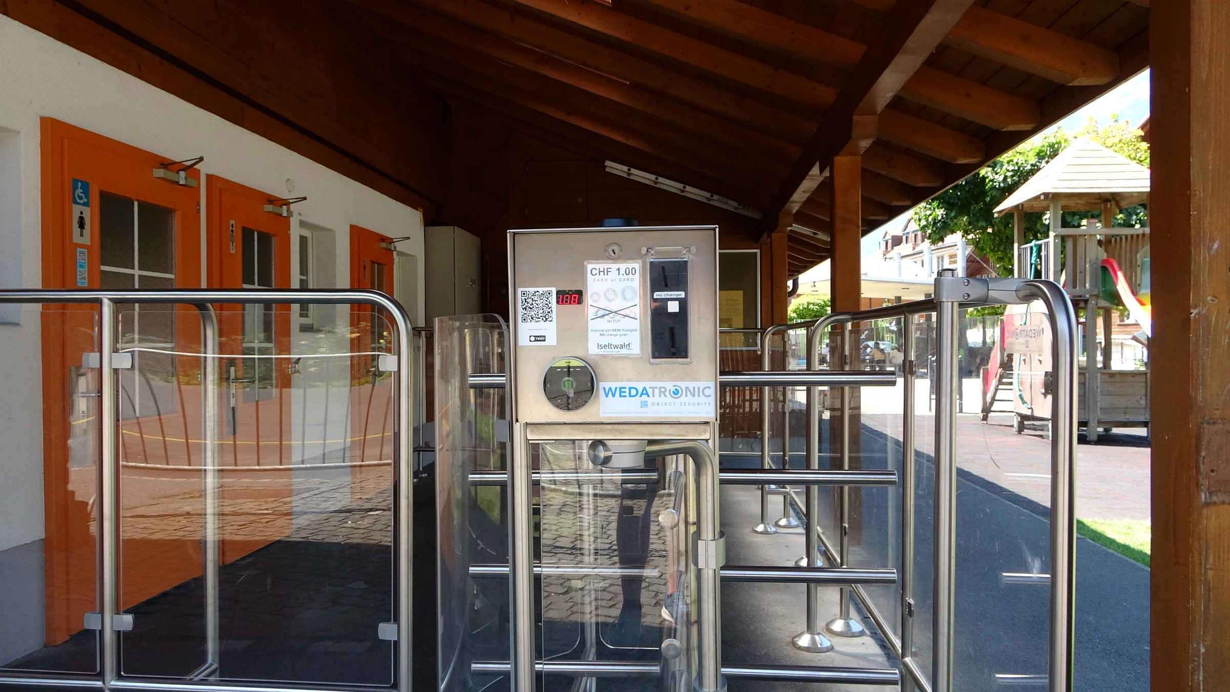 Turnstile with a CHF 1 payment machine in front of the public toilets on the Dorfplatz of Iseltwald