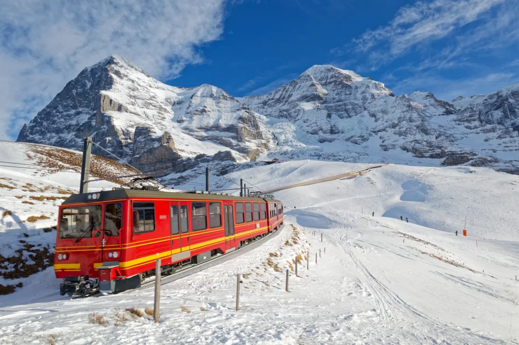 Rote Zahnradbahn der Jungfraubahn im tiefen Schnee mit Eiger und Mönch dahinter
