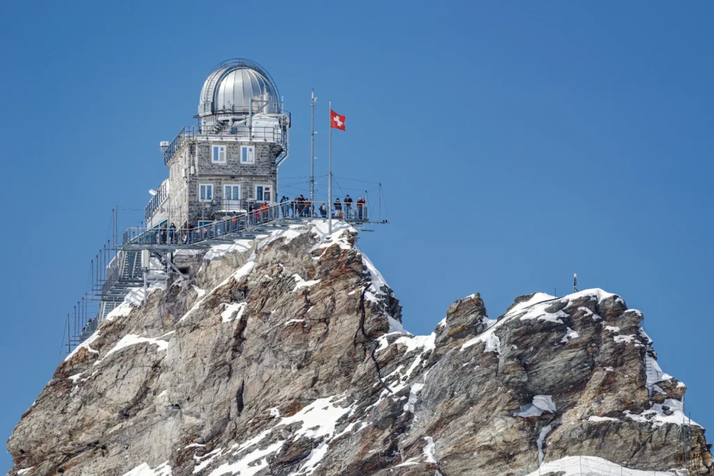 Sphinx Observatory on its rocky peak at the Jungfraujoch with a Swiss flag under a deep blue sky