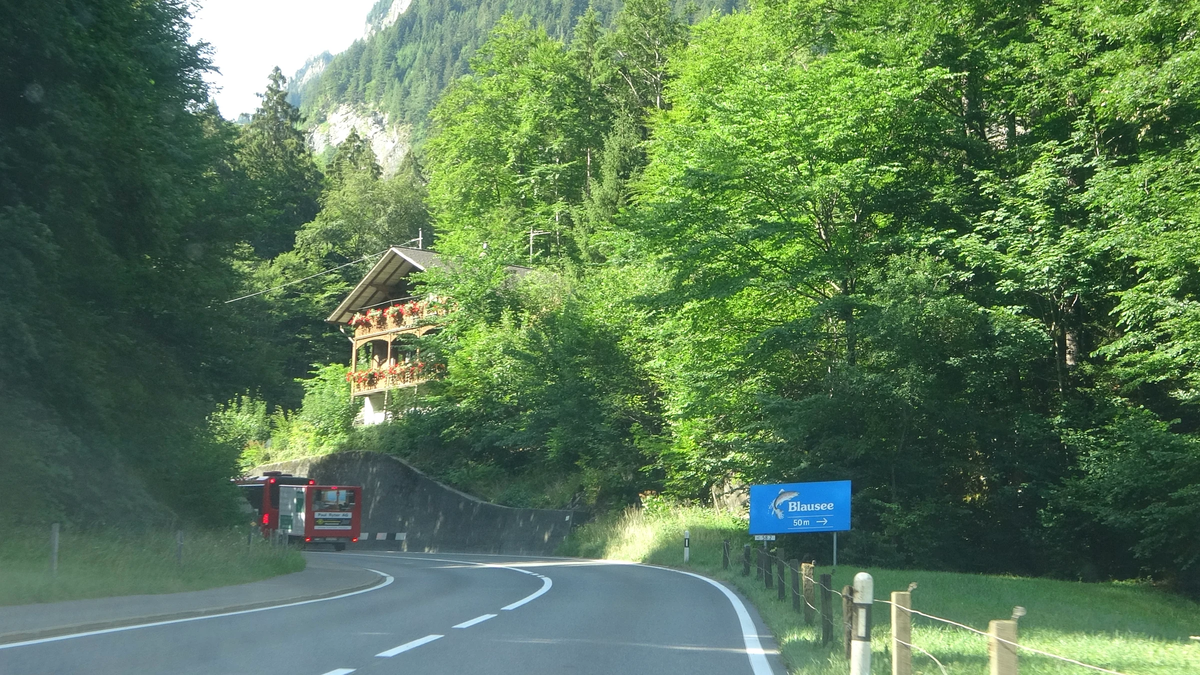 Road through the forest in the Kander Valley with a blue signpost to the Blausee