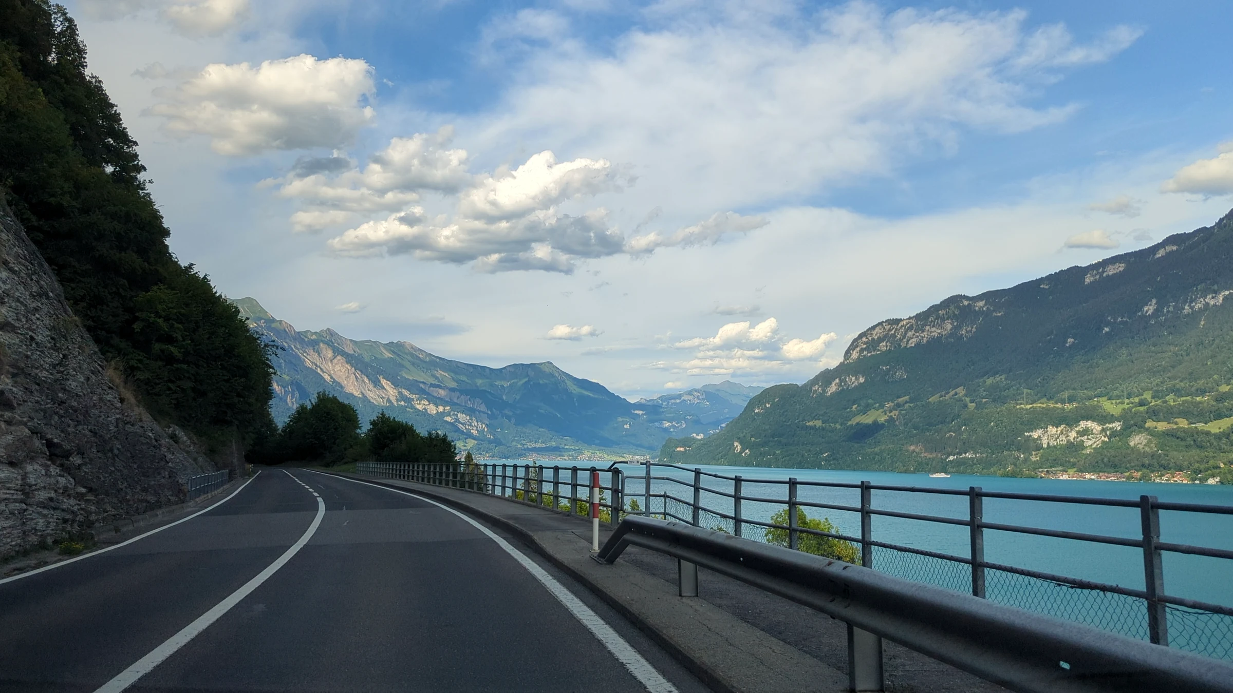 Uferstrasse am Brienzersee mit Geländer, türkisem Wasser und Bergen unter bewölktem Abendhimmel
