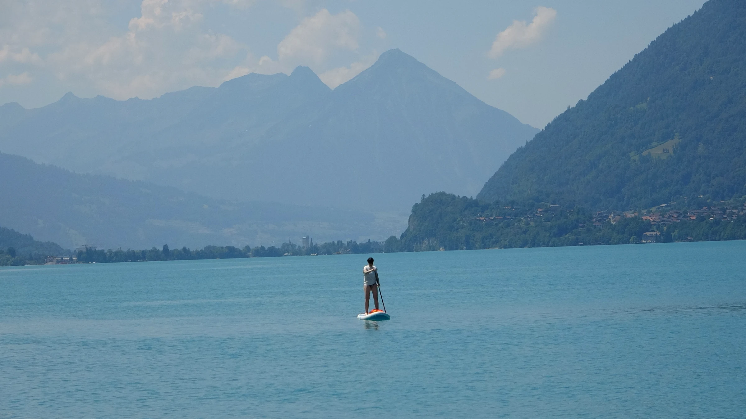 Stand-up-Paddler allein auf dem ruhigen türkisen Brienzersee vor dunstigen Bergen