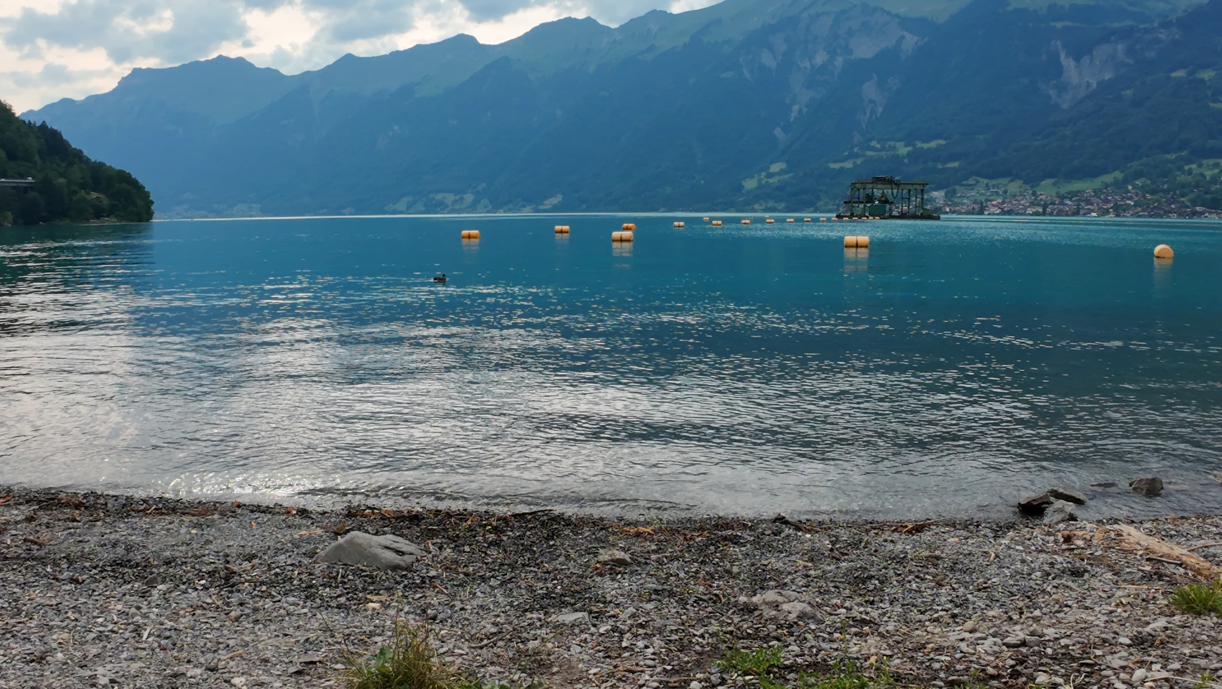 Klares türkisfarbenes Flachwasser am Strand Wycheley mit gelben Bojen und Bergen unter Wolken