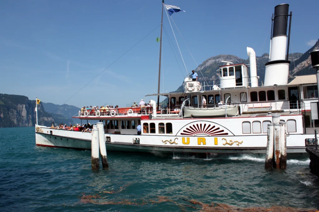 White paddle steamer Uri with passengers on deck at a landing on Lake Lucerne with mountains behind