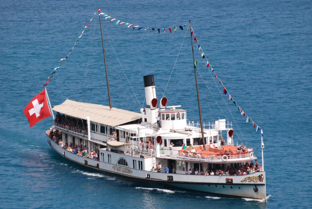 White paddle steamer Stadt Luzern with flags and a Swiss flag at the stern cruising on deep blue Lake Lucerne