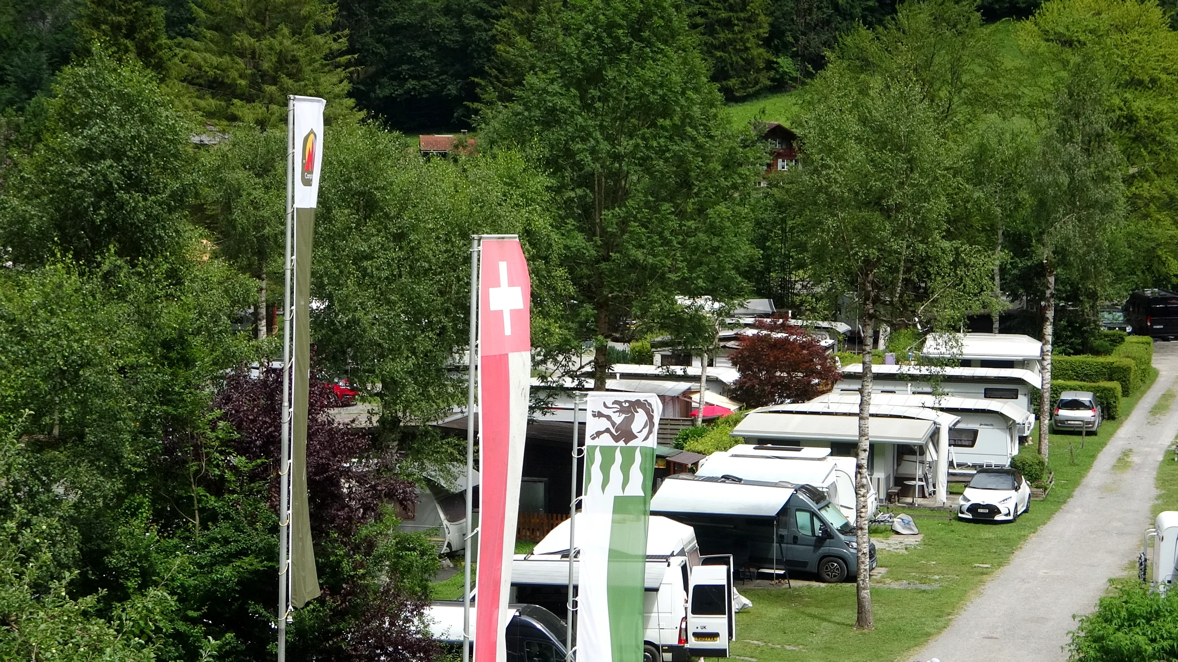 Campsite on the Lauterbrunnen Valley floor with camper vans, caravans, trees and tall flags