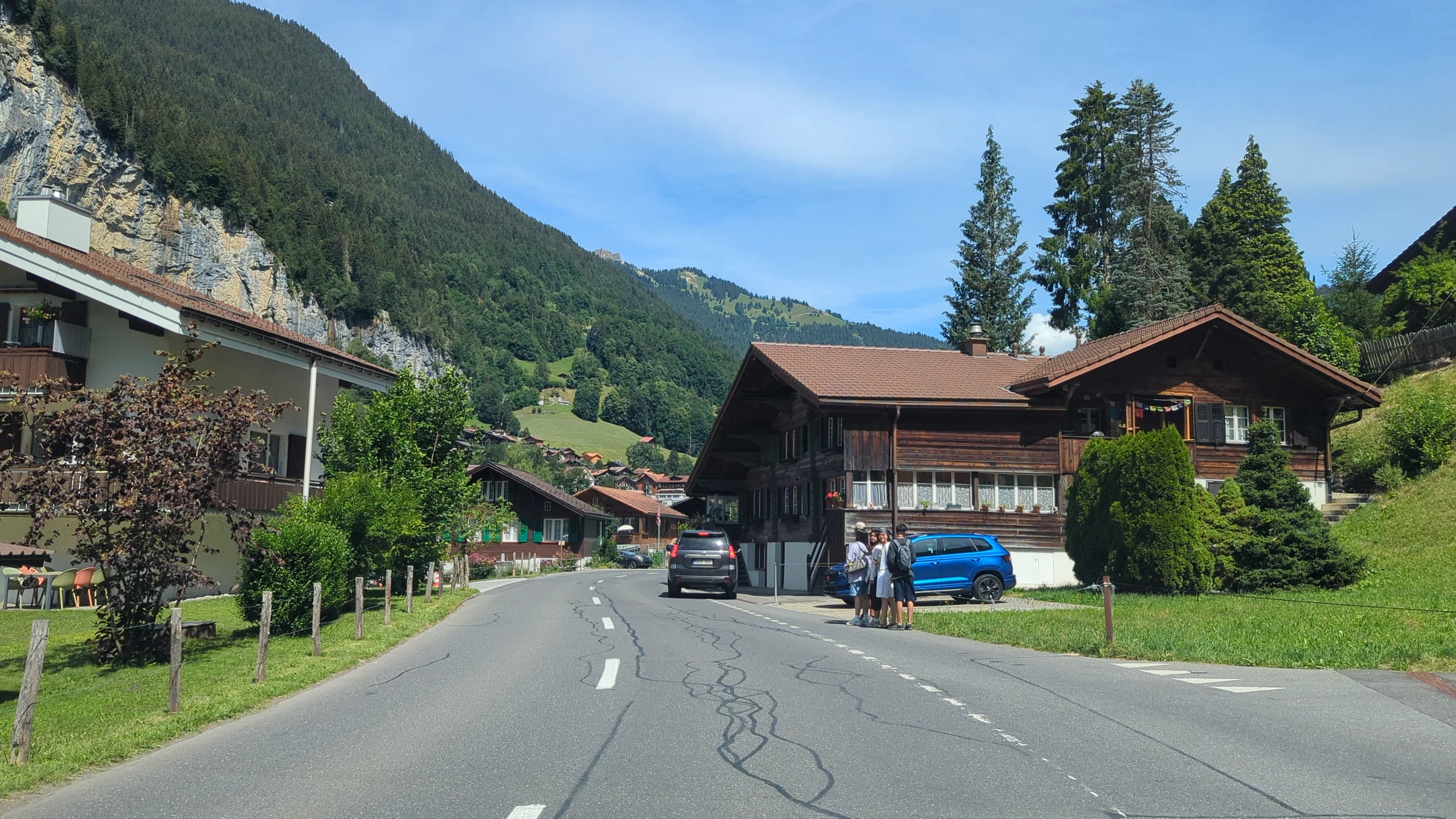 Road into Lauterbrunnen with wooden chalets, gardens and the forested valley side under a blue sky