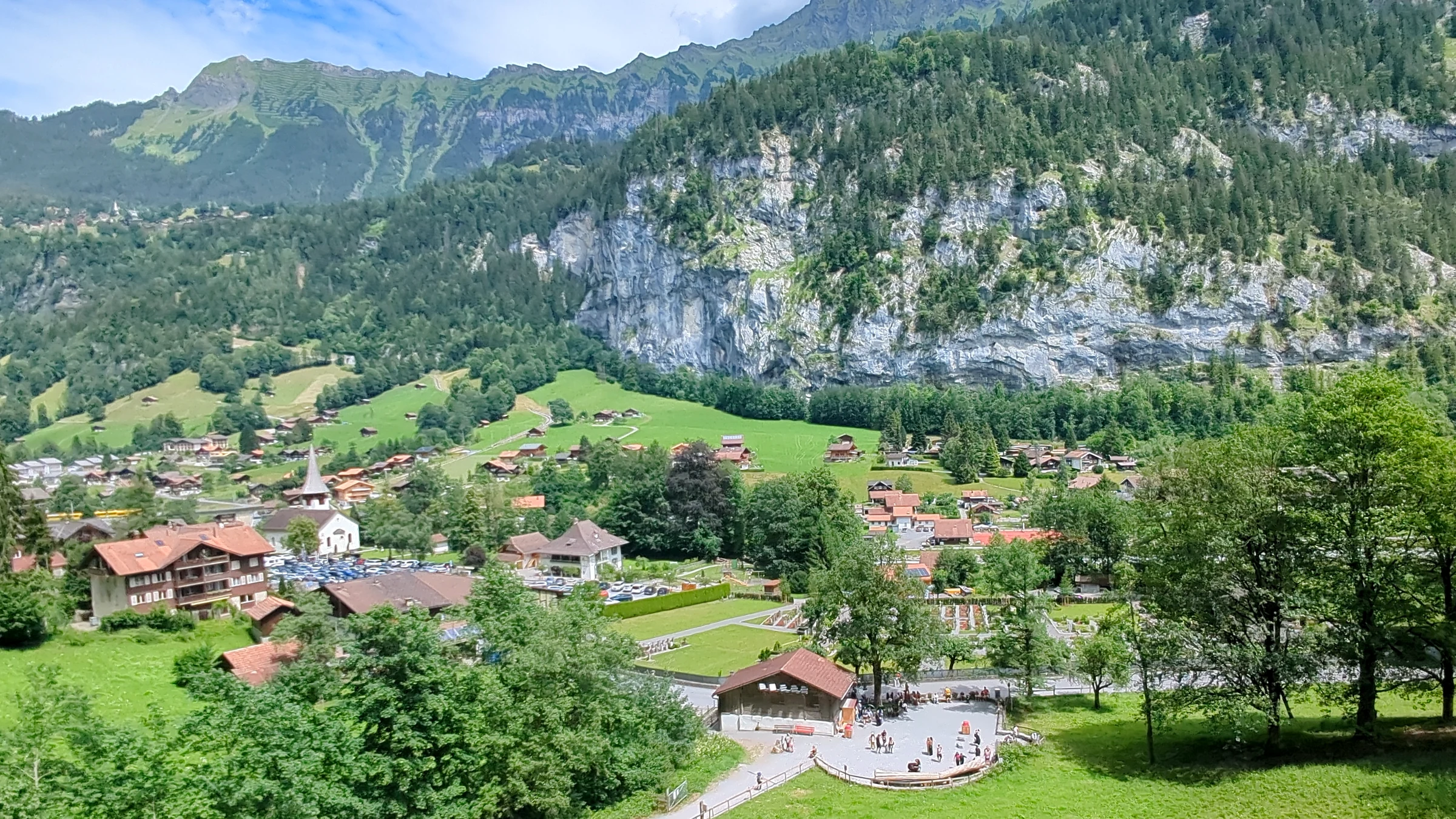 Lauterbrunnen village seen from the slope above, with the church, chalets, meadows and the rock wall behind
