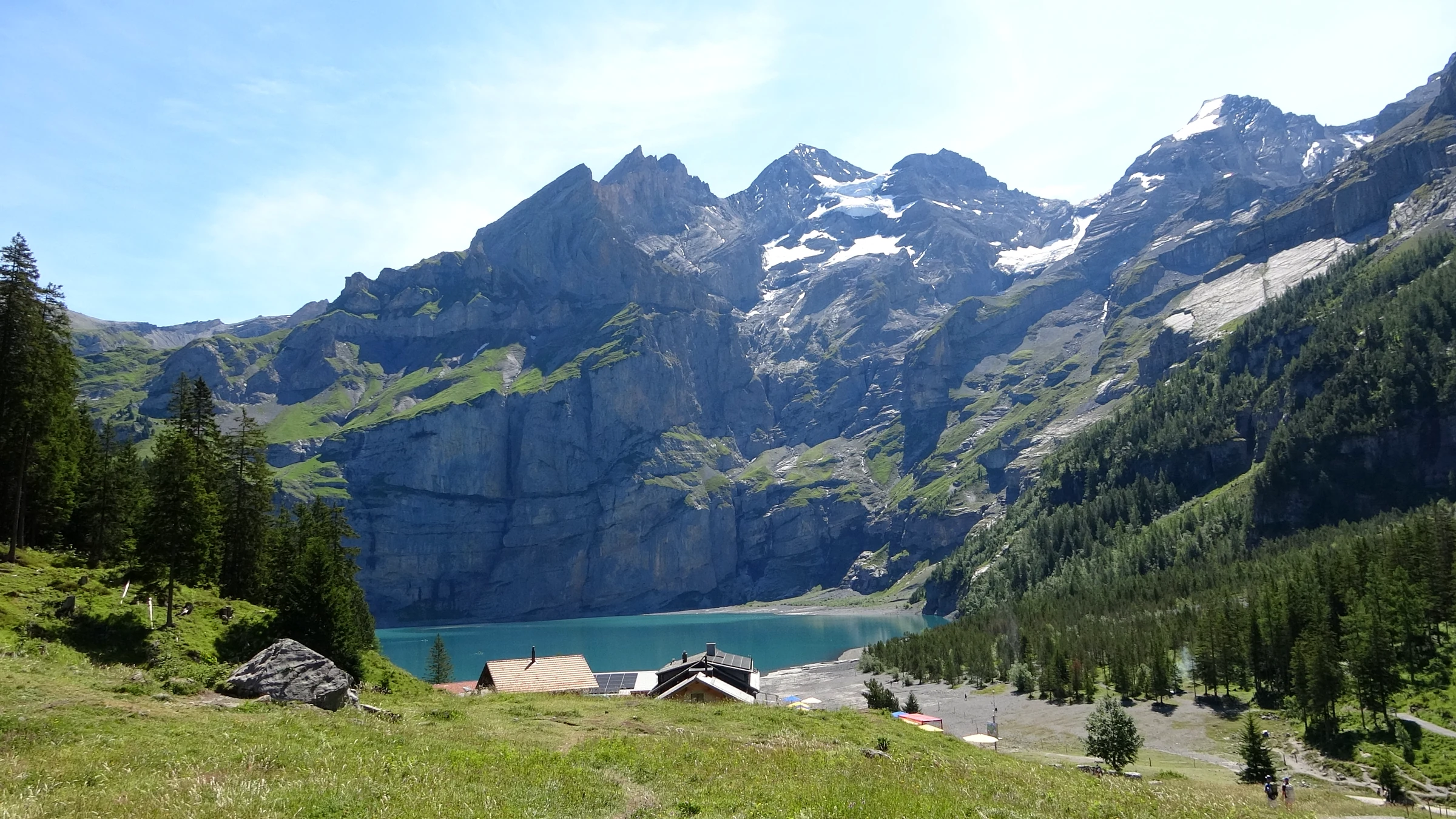 Erster Blick auf den Oeschinensee vom Panoramaweg mit den Dächern des Bergrestaurants am Ufer