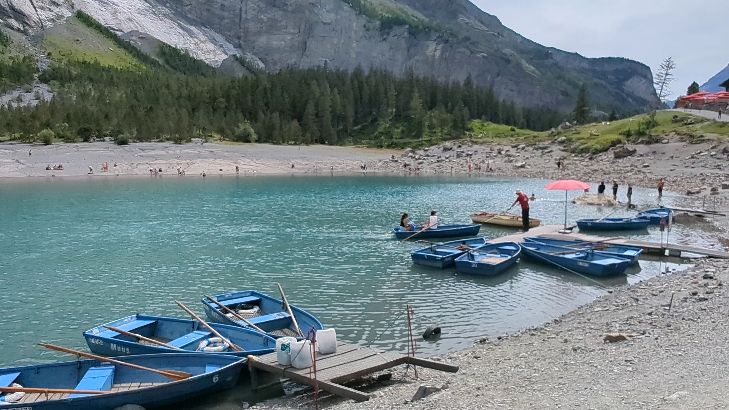 Blaue Ruderboote am Holzsteg des Oeschinensees unter bewölktem Nachmittagshimmel