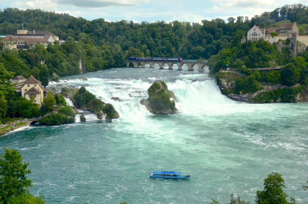 Rhine Falls with turquoise water, the rocks in the middle, the railway bridge and Schloss Laufen on the hill