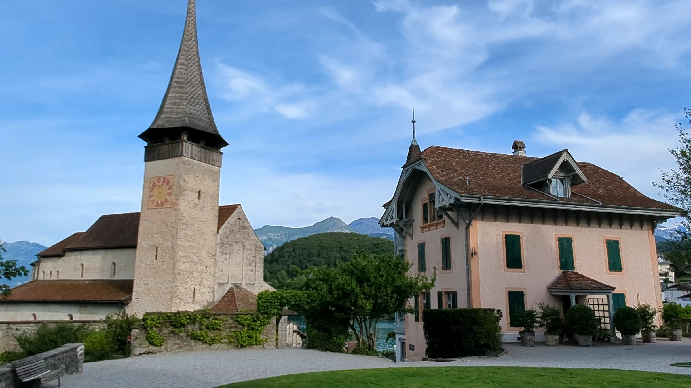 Schlosskirche Spiez mit spitzem Turm neben dem rosa Pfarrhaus mit grünen Fensterläden