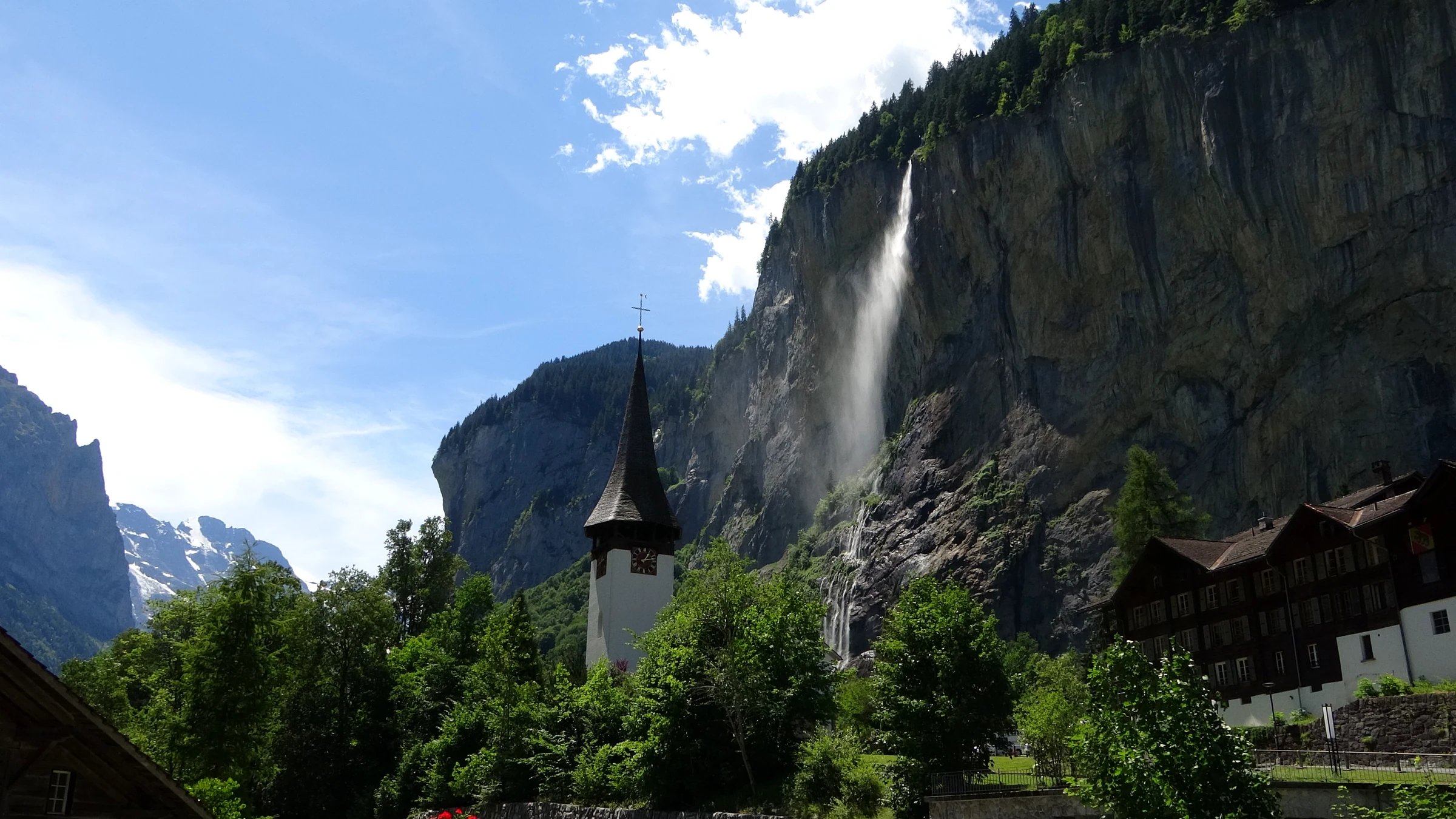 Spitzer Kirchturm von Lauterbrunnen unter dem Staubbachfall mit Chalets und Bäumen