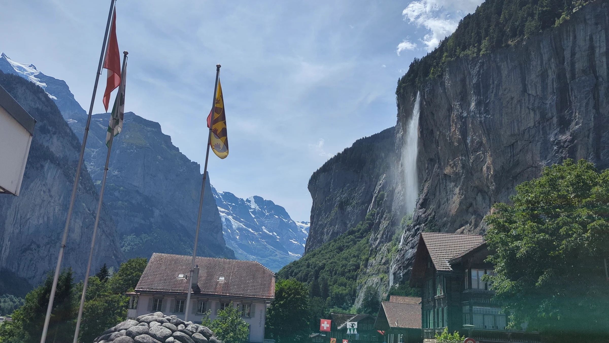 Schweizer und Berner Fahne vor dem Staubbachfall und verschneiten Bergen am Ende des Lauterbrunnentals