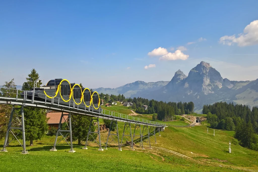 Cylindrical cabins of the Stoos funicular on the steel track, with the twin Mythen peaks behind