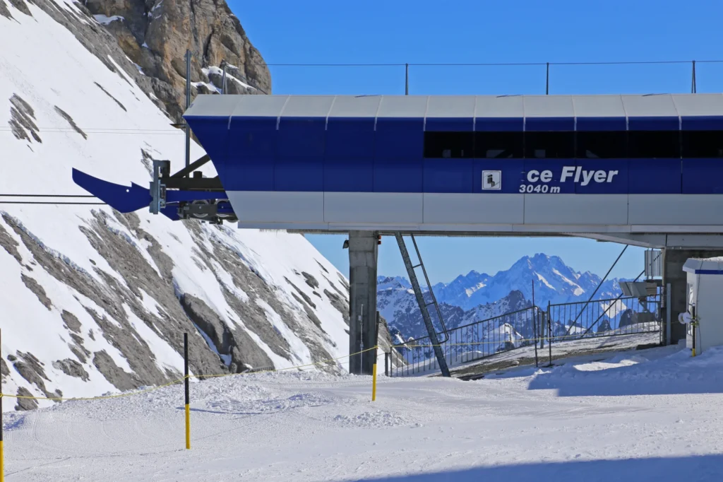 Blaue Bergstation des Sessellifts Ice Flyer auf 3040 Metern am Titlisgletscher, dahinter Schneehänge und Gipfel