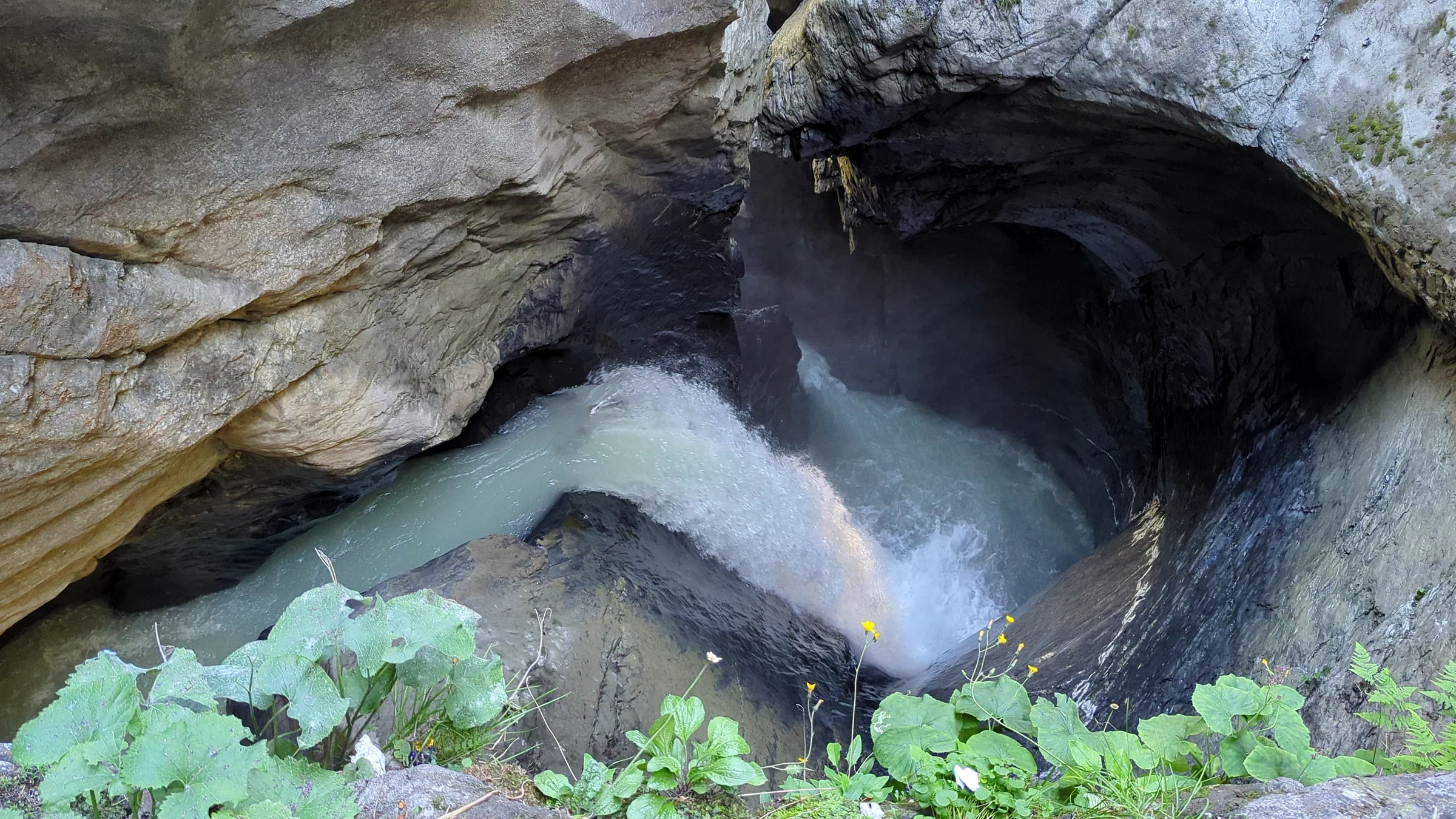 Wasserfall stürzt in ein rundes Becken unter einem Felsüberhang in der Trümmelbachschlucht